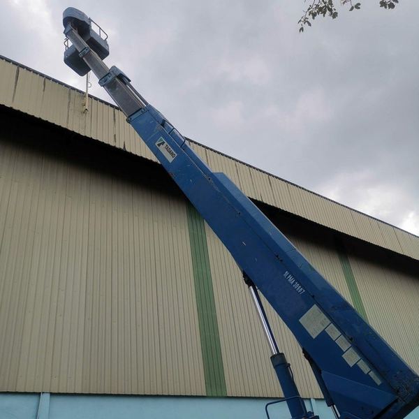 Tadano boom lift extended towards a warehouse roofline under a grey sky