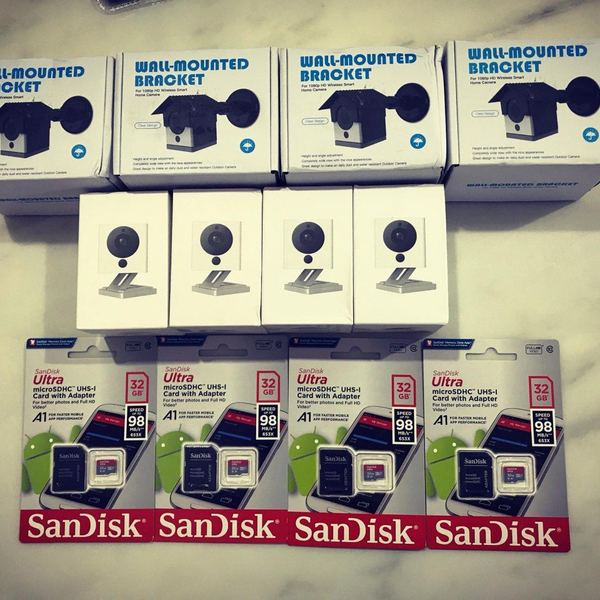 Four smart home cameras laid out with wall-mount brackets and memory cards, ready for installation