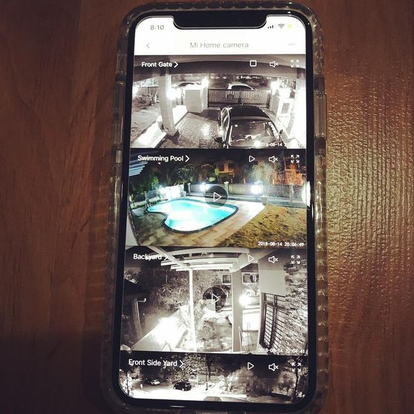 Phone showing four live home CCTV feeds labelled front gate, swimming pool, backyard and front side yard