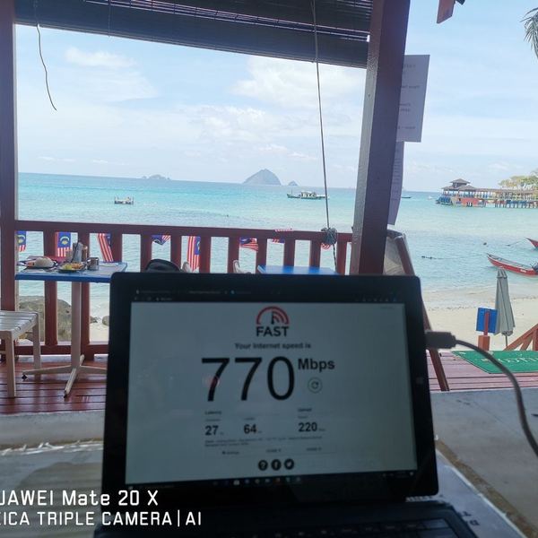 Laptop on a beachfront table showing a 770 Mbps speed test result, with an island jetty and boats behind