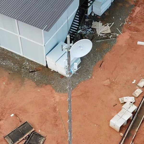 Overhead drone view of a lattice mast carrying a dish and radios beside a site office under construction